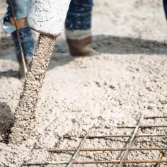 Półsuchy beton na wylewkę płynie z rury, tworząc solidną podstawę dla budowy. Robotnicy w gumowcach nadzorują proces.