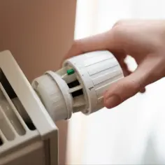 Dłoń reguluje termostat grzejnika. Kaloryfer nie grzeje, a nie jest zapowietrzony, co frustruje domowników.