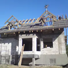 Na dachu budowy domu z betonu komórkowego widać drewnianą konstrukcję i wiechę.