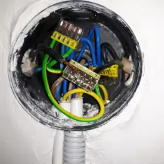 Instalacja elektryczna w puszce: jak podłączyć gniazdko w starej instalacji? Widoczne przewody: fazowy (czarny), neutralny (niebieski), ochronny (żółto-zielony) połączone złączkami.