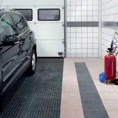 Nowoczesny garaż z czarnym SUV-em i czerwonym urządzeniem. Zastanawiasz się, jakie płytki do garażu wybrać? Tutaj widzisz kratkę i płytki.