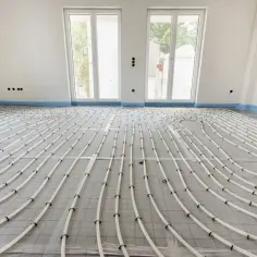 Instalacja ogrzewania podłogowego w bloku. Białe rurki ułożone na siatce izolacyjnej tworzą skomplikowany wzór, zapowiadając komfort cieplny.