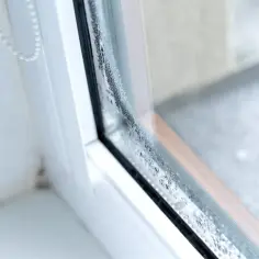 Krople wody na szybie okna, tworzące smugi i zacieki. Woda na oknach świadczy o kondensacji.
