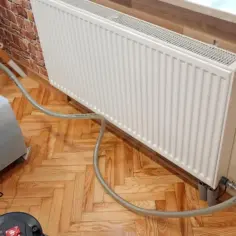 Profesjonalne czyszczenie instalacji co. Pompa do płukania grzejników podłączona do białego grzejnika, gotowa do pracy.