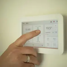 Dłoń dotyka ekranu termostatu, pokazując temperaturę 19,5°C. Ustawienia ogrzewania pomogą określić, jak często powinien włączyć się piec gazowy.