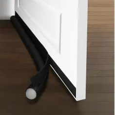 Czarny materiałowy wałek z rzepem, który pomaga jak uszczelnić drzwi wejściowe, leży na drewnianej podłodze przy białych drzwiach.