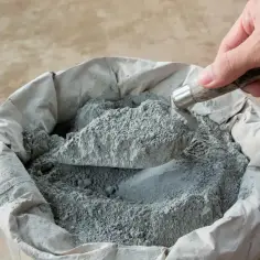Łopata nabiera suchy beton z worka. Materiał budowlany czeka na zmieszanie z wodą, by stworzyć solidną konstrukcję.