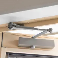 Mechanizm samozamykacza drzwi, widoczny na drewnianej futrynie, zapewnia płynną regulację domykania.