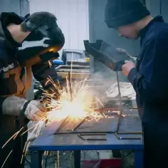 Dwóch spawaczy uczy się, jak spawać spawarka inwertorowa. Iskry lecą podczas pracy.