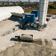 Betoniarnia z silosami i ciężarówką z materiałem. Widać tu elementy do produkcji betonu, kluczowe dla zachowania właściwych **styrobeton proporcji**.