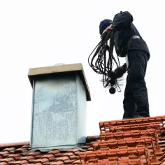Kominiarz na dachu przygotowuje narzędzia, by sprawdzić, jak ustawić szyber w piecu.