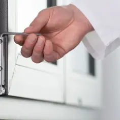 Dłoń reguluje zawias okna za pomocą klucza imbusowego, poprawiając docisk.
