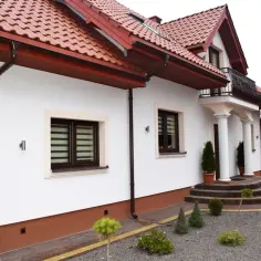 Elegancki cokół na elewacji domu, podkreślony brązowymi rynnami i ozdobnymi schodami.