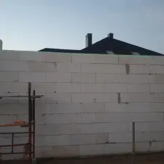 Laserowy pomiar poziomu pomaga jak wyrównać bardzo krzywe ściany z bloczków. W tle dach domu.