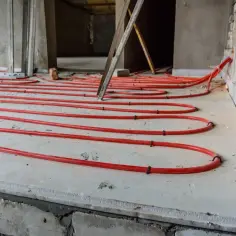 Układanie rur ogrzewania podłogowego na styropianie. Widać czerwone rurki ułożone w pętle, przygotowane do zalania wylewką.