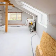 Wnętrze w trakcie rozbudowy domu. Widać rusztowania, materiały budowlane, okna i instalacje elektryczne.