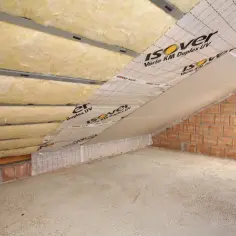 Izolacja poddasza wełną mineralną. Widać warstwy wełny, folię paroizolacyjną Isover Vario KM Duplex UV i ściany z cegły.