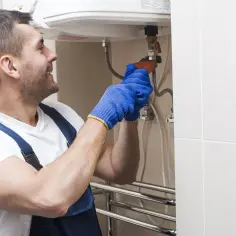 Instalator w niebieskich rękawiczkach dokręca zawór, pokazując, jak spuścić wodę z bojlera.