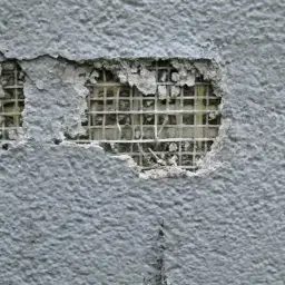 Uszkodzony tynk odsłania siatkę, która wygląda jak pułapka na muchy. Zatapianie siatki błędy to proces, który może prowadzić do takich uszkodzeń.