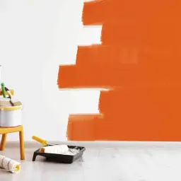 Narzędzia malarskie i farba w trakcie malowania ściany na pomarańczowo. Szukasz najlepsza farba do ścian ranking?