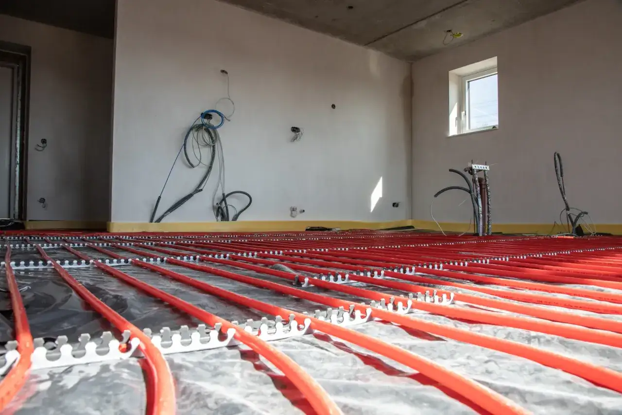 Instalacja ogrzewania podłogowego w garażu, przygotowana do wylania posadzki. Czerwone rurki ułożone na folii izolacyjnej.