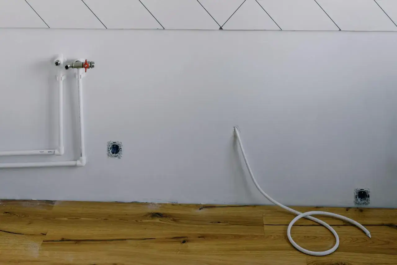 Białe rury wodne i zawór na ścianie, przygotowanie do instalacji gazowej w domu. Podłoga z drewna.
