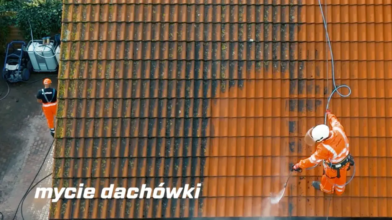 Usuwanie mchu z dachu. Pracownik w pomarańczowym stroju czyści dach myjką ciśnieniową, przywracając mu dawny blask.