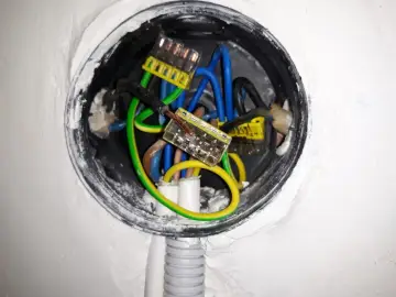 Instalacja elektryczna w puszce: jak podłączyć gniazdko w starej instalacji? Widoczne przewody: fazowy (czarny), neutralny (niebieski), ochronny (żółto-zielony) połączone złączkami.