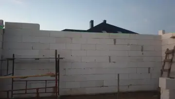 Laserowy pomiar poziomu pomaga jak wyrównać bardzo krzywe ściany z bloczków. W tle dach domu.
