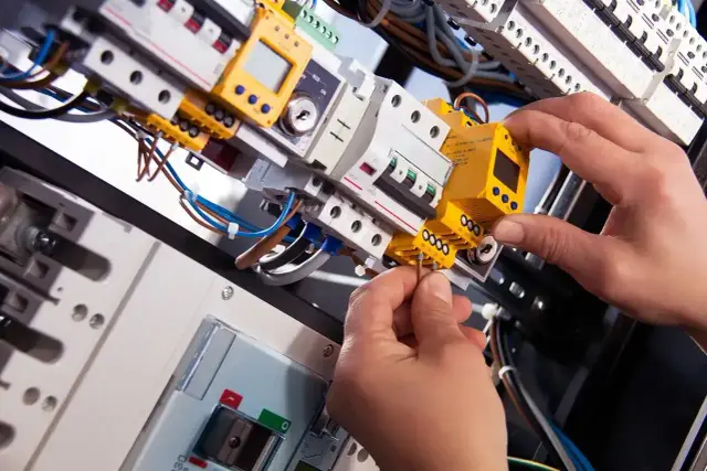 Ręce montują żółty moduł w skrzynce elektrycznej. Praktyczne ćwiczenie z kursu elektryka od podstaw.